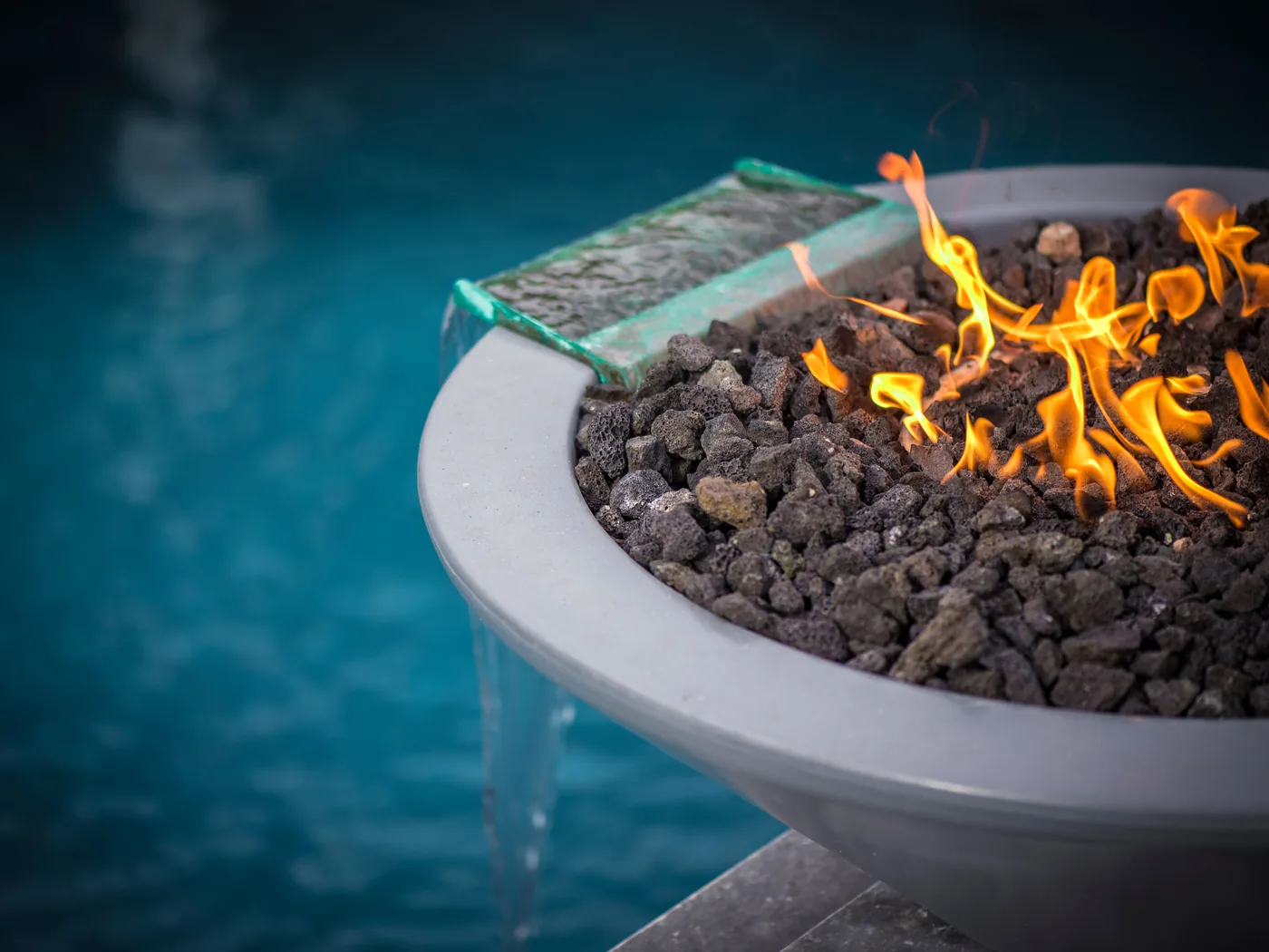 A The Outdoor Plus fire and water bowl, flame burning across the top while water spills from the lip into the pool below